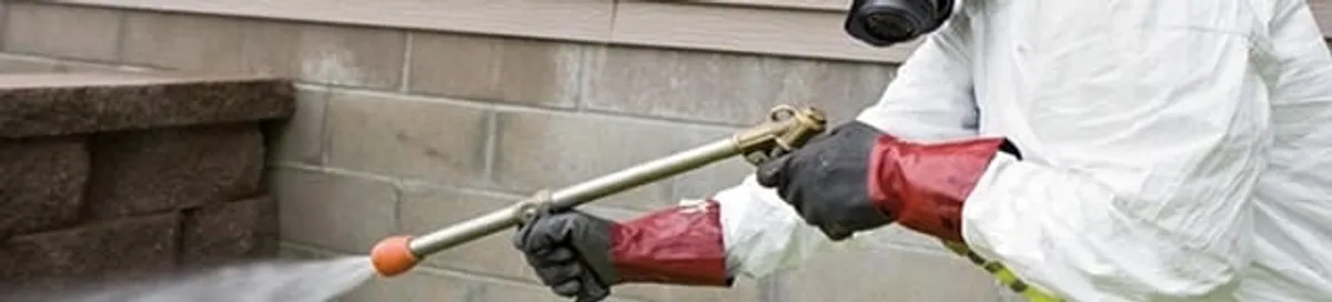 Pest control technician applying exterior insect treatment along a home foundation in Fort Wayne, IN