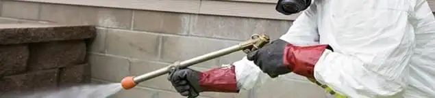 Pest control technician applying exterior insect treatment along a home foundation in Fort Wayne, IN