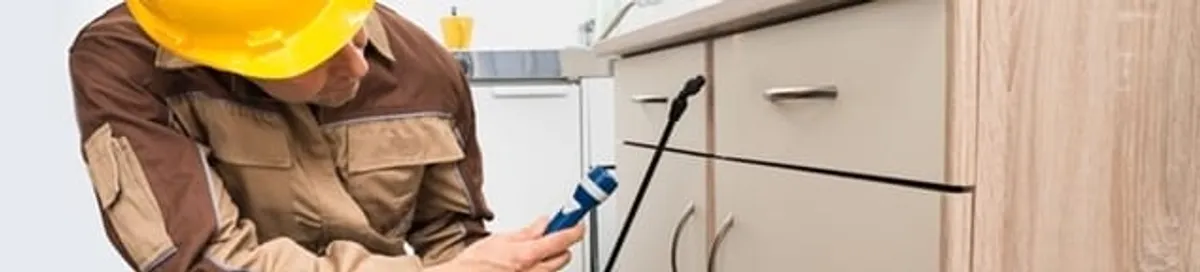 Roach exterminator applying treatment under kitchen cabinets in Fort Wayne, IN