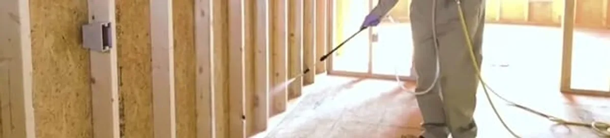 Termite treatment technician applying spray along framing and unfinished walls in Fort Wayne, IN