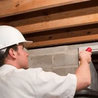 Termite inspection technician checking a basement wall and framing for termite activity in Fort Wayne, IN